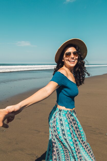 Mujer con sonrisa feliz sosteniendo la mano del hombre y caminando en la playa