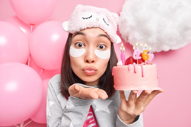 mujer sopla aire beso en la cámara mantiene los labios doblados sostiene la torta festiva con velas encendidas se prepara para las celebraciones aplica parches de belleza