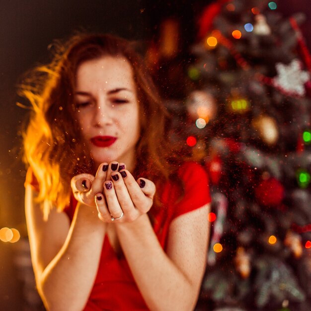 La mujer sopla la nieve de sus palmas que se colocan antes del árbol de navidad