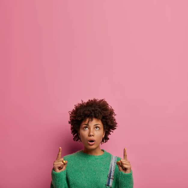 Mujer sorprendida confundida con peinado afro, apunta hacia arriba