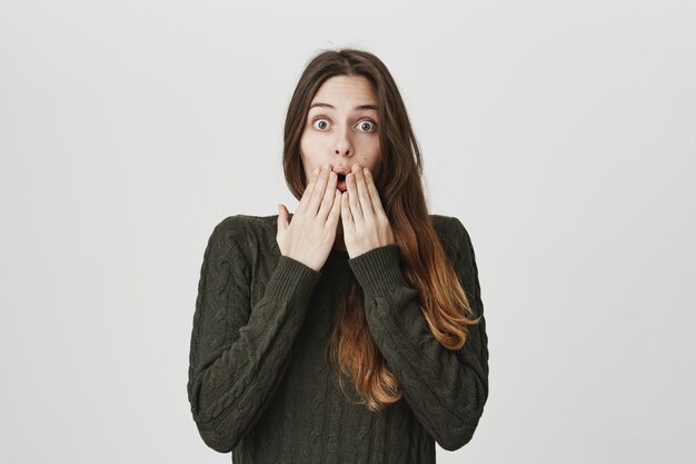 Mujer sorprendida e impresionada escucha noticias increíbles, toma las manos cerca de la boca