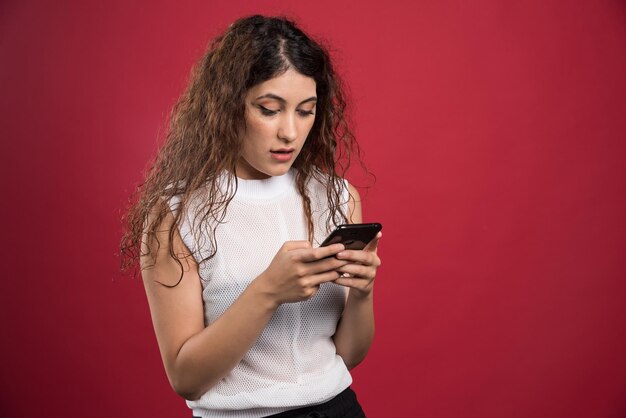 Mujer sorprendida está escribiendo algo en su teléfono móvil en rojo