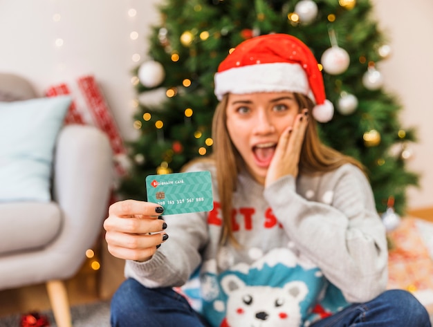 Mujer sorprendida en gorro navideño con tarjeta de crédito.