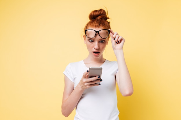 Mujer sorprendida de jengibre mirando el teléfono inteligente