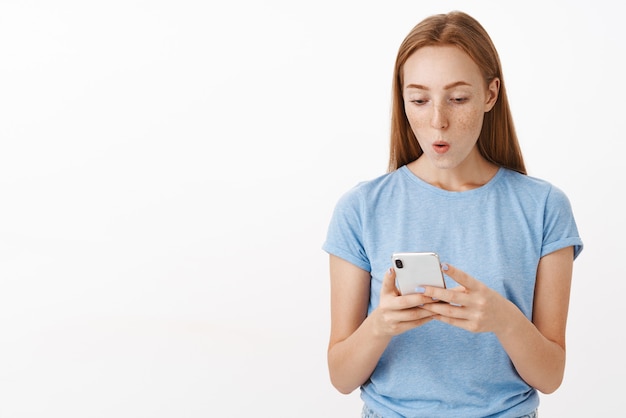 Mujer sorprendida mirando la pantalla del teléfono inteligente mientras sostiene el teléfono con ambas manos