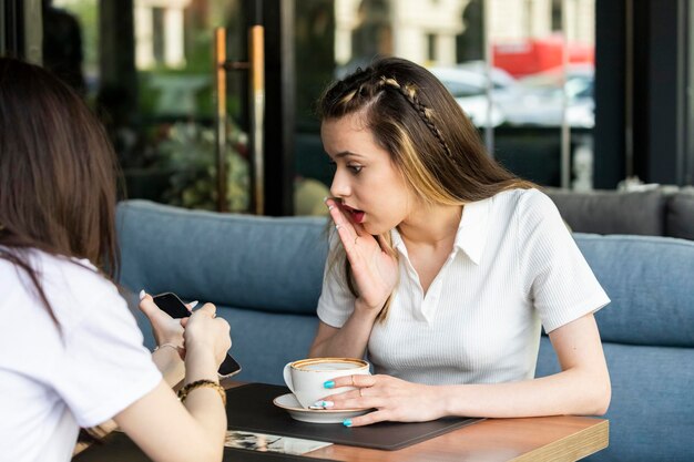 Mujer sorprendida mirando el teléfono de su amiga