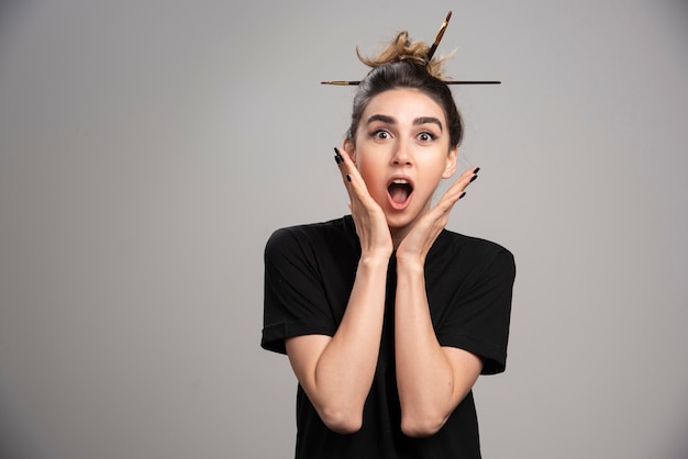 Foto gratuita mujer sorprendida con moño desordenado posando en la pared gris.