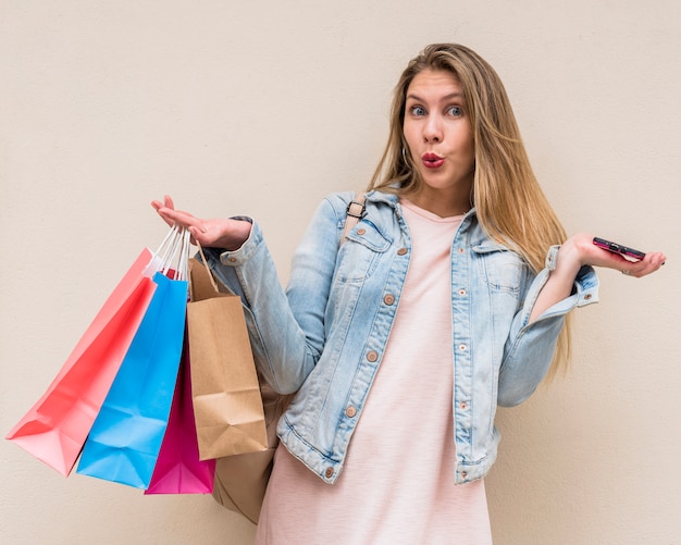 Foto gratuita mujer sorprendida de pie con bolsas y teléfono inteligente