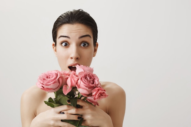 Mujer sorprendida de pie desnuda y sosteniendo un ramo de rosas