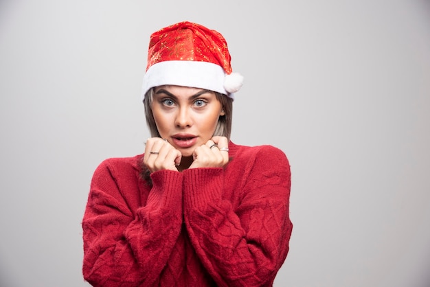 Mujer sorprendida en pie de sombrero de Santa sobre fondo gris.