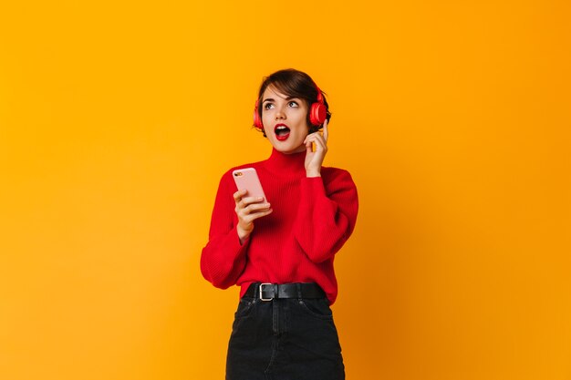 Mujer sorprendida posando con auriculares y smartphone