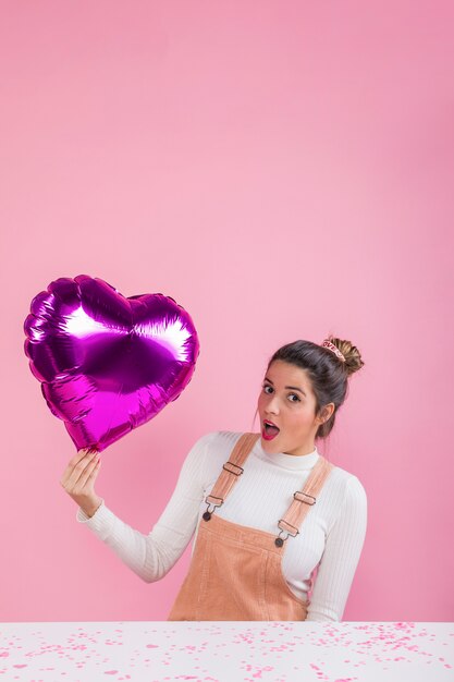 Mujer sorprendida que sostiene el globo del corazón en la mano