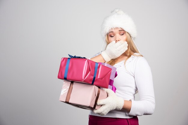 Mujer sorprendida que sostiene los regalos de Navidad en la pared gris.