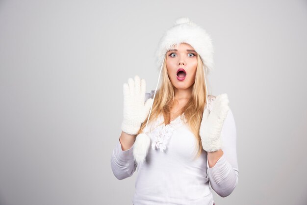 Mujer sorprendida con sombrero blanco y suéter blanco.