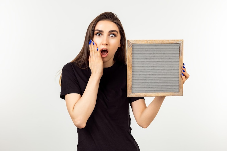 Foto gratuito mujer sorprendida sosteniendo el tablero y mirando a la cámara con la boca abierta