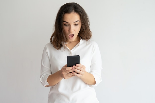 Foto gratuita mujer sorprendida sosteniendo teléfono inteligente y mirando su pantalla