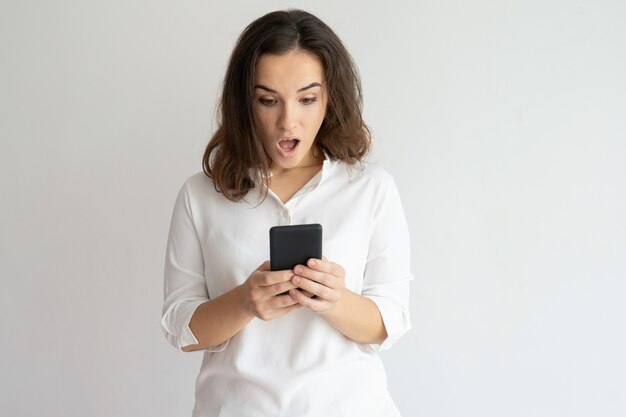 Mujer sorprendida sosteniendo teléfono inteligente y mirando su pantalla