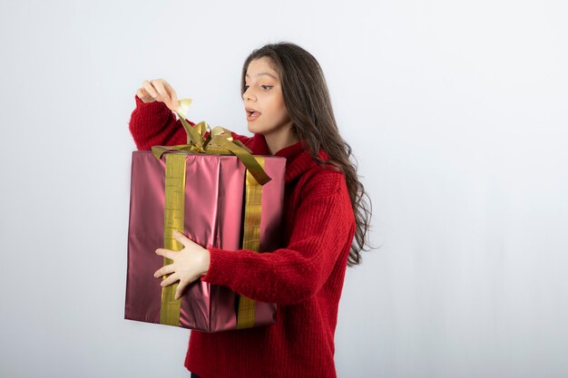 Mujer sorprendida en suéter rojo abriendo una caja de regalo de Navidad.