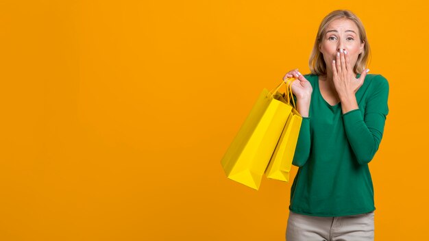 Mujer sorprendida tapándose la boca mientras sostiene muchas bolsas de la compra con espacio de copia