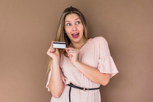 Mujer sorprendida en vestido de pie con tarjeta de crédito.