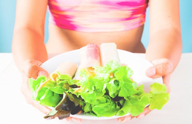 Mujer en sostén deportivo sosteniendo un plato de ensalada después de ejercicios de entrenamiento de fitness en día de verano. Concepto de estilo de vida saludable y saludable