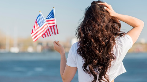 Foto gratuita mujer sosteniendo 2 banderas de estados unidos desde atrás