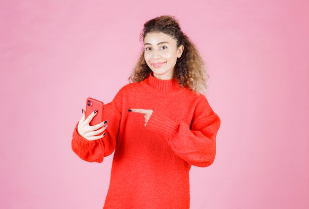 mujer sosteniendo y apuntando a su nuevo teléfono inteligente de marca.