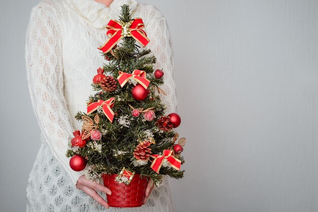 Mujer sosteniendo un árbol de Navidad decorado con adornos rojos