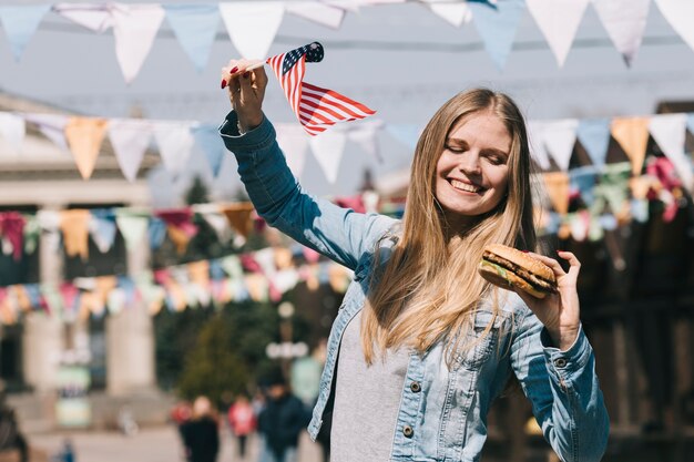 Mujer sosteniendo bandera estadounidense y hamburguesa sabrosa