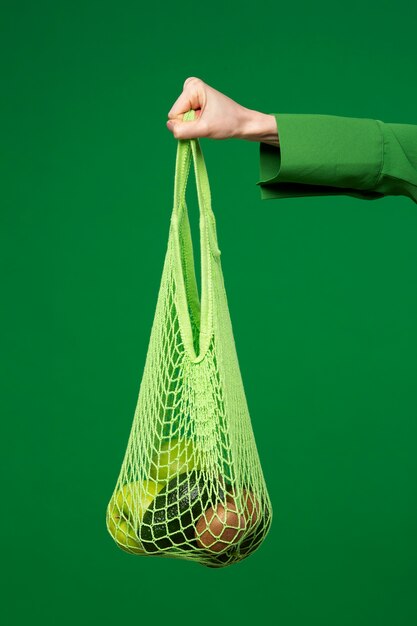 Mujer sosteniendo una bolsa de malla con manzanas, aguacate y kiwi