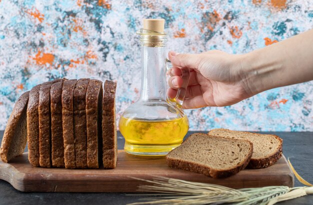 Mujer sosteniendo la botella de aceite sobre la mesa de mármol con rebanadas de pan.