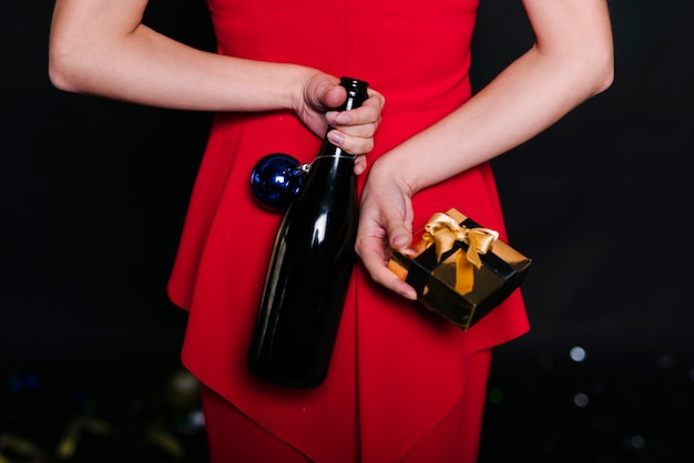 Mujer sosteniendo una botella con una caja de regalo detrás de la espalda