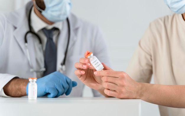 Mujer sosteniendo una botella de vacuna junto al médico