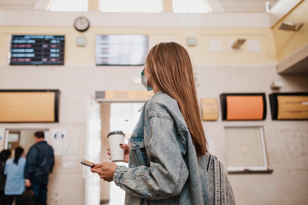 Mujer sosteniendo café y estar en una estación de tren