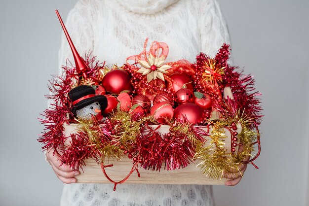 Mujer sosteniendo una caja de adornos navideños rojos