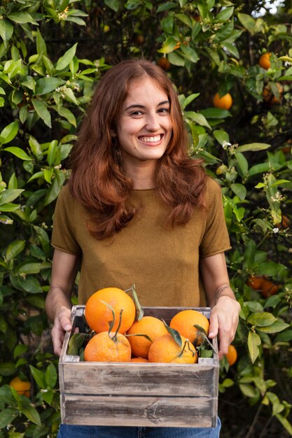 Mujer sosteniendo una caja llena de naranjas en sus manos