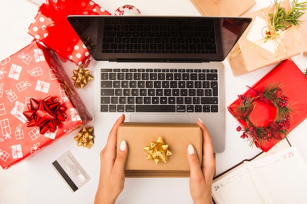 Mujer sosteniendo una caja de regalo mientras compra en línea en la mesa con la decoración de Navidad