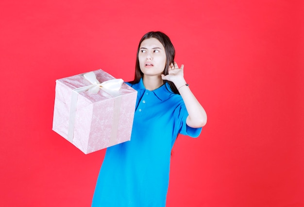 mujer sosteniendo una caja de regalo morada y llamando a alguien para que venga a recibirla.