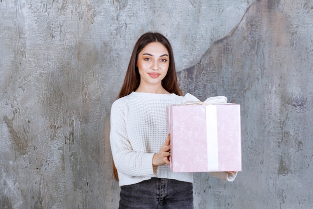 mujer sosteniendo una caja de regalo púrpura envuelta con cinta blanca.