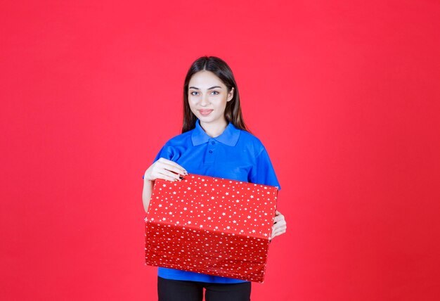 mujer sosteniendo una caja de regalo roja con puntos blancos.