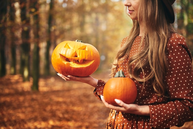 Mujer sosteniendo calabaza de halloween en el bosque de otoño