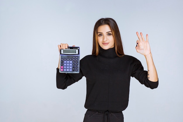 mujer sosteniendo una calculadora azul y disfrutando del resultado final.