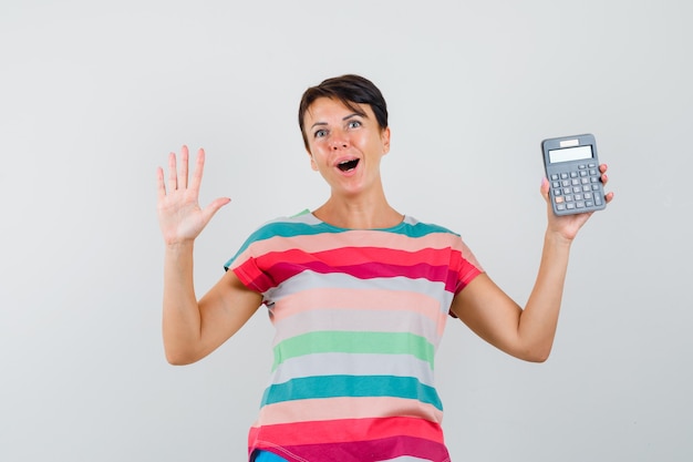 Mujer sosteniendo calculadora, mostrando la palma en camiseta a rayas y mirando feliz