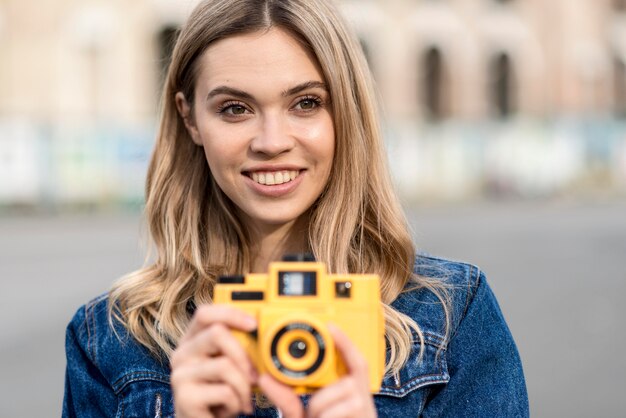Mujer sosteniendo una cámara amarilla retro al aire libre
