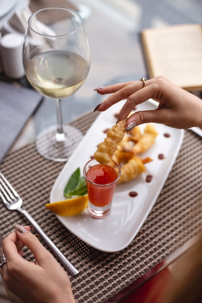 Una mujer sosteniendo camarones con salsa de chile dulce rodaja de limón y un vaso de vino blanco sobre la mesa