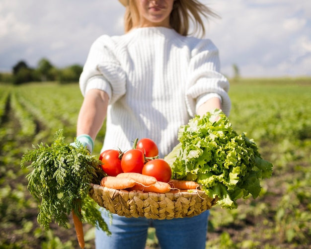 Mujer sosteniendo una canasta llena de verduras delante de ella