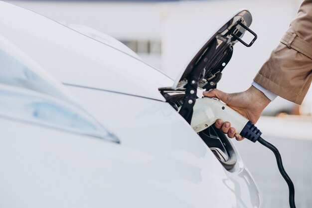 Mujer sosteniendo el cargador y el coche eléctrico de carga de cerca