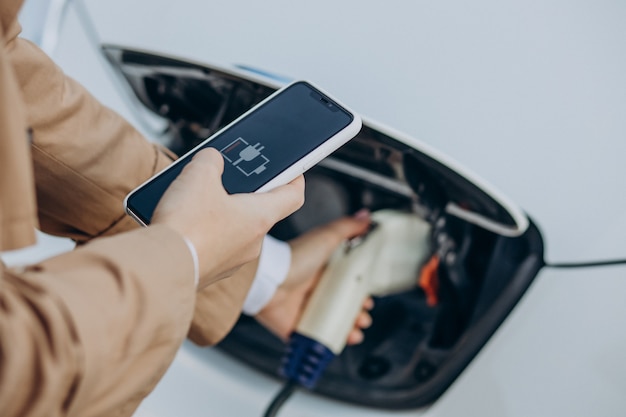 Mujer sosteniendo el cargador y el coche eléctrico de carga de cerca