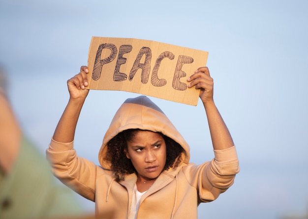 Foto gratuita mujer sosteniendo un cartel de paz de cerca