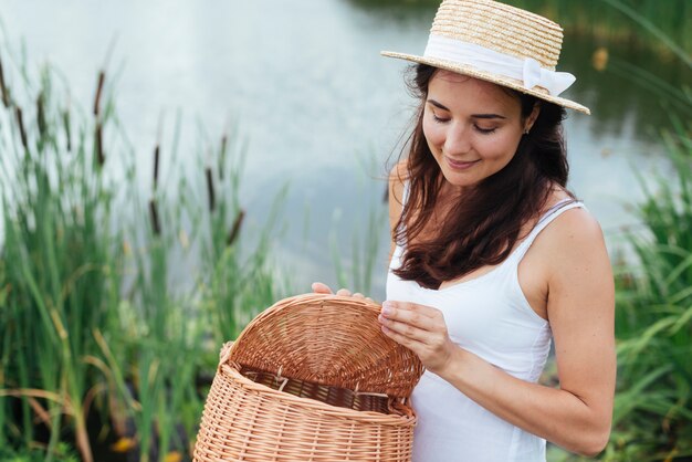 Mujer sosteniendo cesta de picnic junto al lago